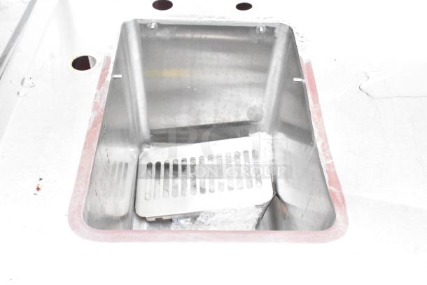 Stainless steel single bay sink with backsplash and under shelf, used condition, features slotted insert.