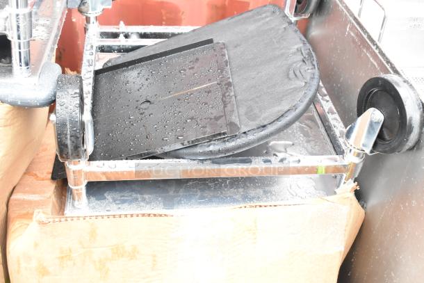 Stacked items with metal frames and wheels, partially unpacked in a cardboard box, showing wet surfaces.