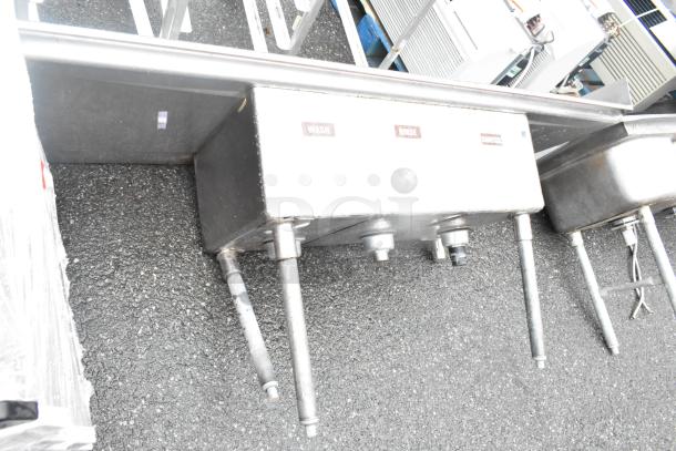 Stainless steel 3 bay sink with dual drain boards; in used condition, missing 1 leg. Labeled: Wash, Rinse, Sanitize.