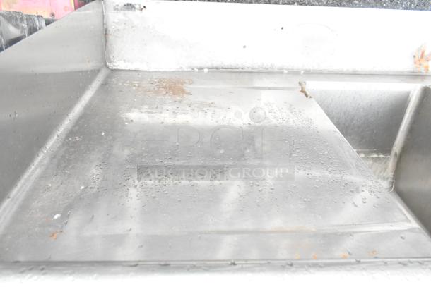 Stainless steel 3 bay sink with dual drain boards, missing one leg, visible water spots, moderate wear.