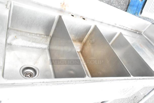 Stainless steel 3 bay sink with dual drain boards, missing one leg. Visible wear suggests used condition.