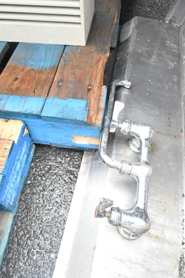 Stainless steel 3 bay sink with faucet, visible wear, missing right legs, on wooden pallet in industrial setting.