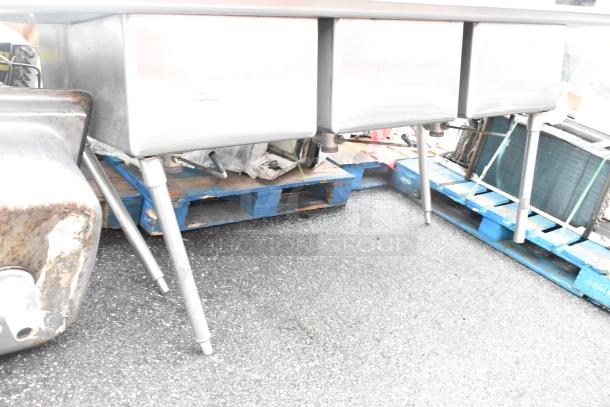 Stainless steel 3 bay sink with dual drain boards, sturdy legs, and signs of general wear. Ideal for commercial use.