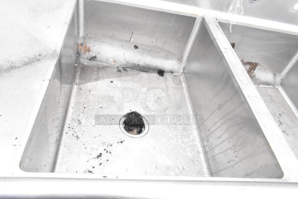 Stainless steel 3 bay sink with dual drain boards, visible wear and debris in basins, suitable for commercial use.