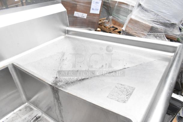 Stainless Steel 3 bay sink with dual drain boards. Features scuffs and marks indicating previous use. Ideal for commercial use.