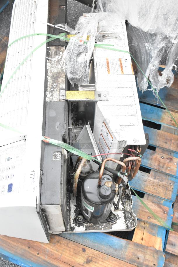 Metal air conditioner unit on wooden pallet, showing wiring and compressor. Appears in used condition with visible wear.