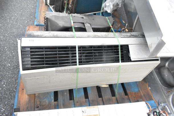 Metal air conditioner unit on wooden pallet, horizontal vents, some surface wear, secured with green straps, labeled "178."