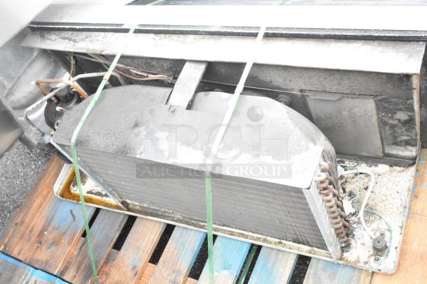 Metal air conditioner unit on wooden pallet, featuring visible coils and wiring. Used condition with surface dust and stains.