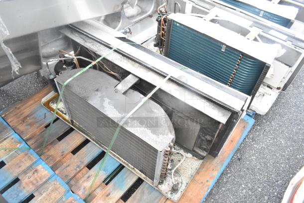 Metal air conditioner on wooden pallet, industrial model, visible coils, piping, and fan unit, moderate wear.