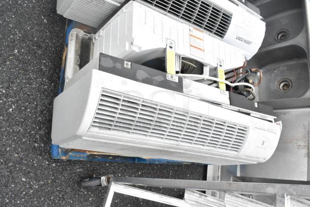 Two used metal air conditioners with visible grilles and labels, showing wear on a pallet. Tags marked "USED ASSET."