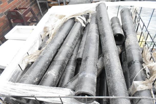 Pallet lot of black poly pipes, various lengths, some wear visible, contained in wire frame with protective wrap.