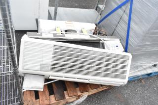 Metal air conditioner on pallet, showing front grille and control panel. Some wear visible; cords attached.