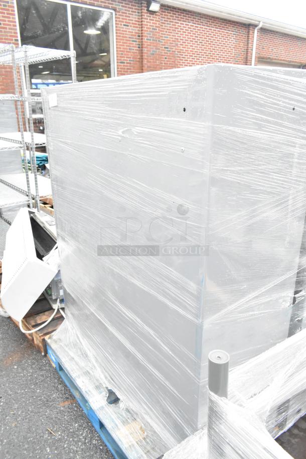 Two gray metal cabinets wrapped in plastic, placed on a pallet, appear in new condition.