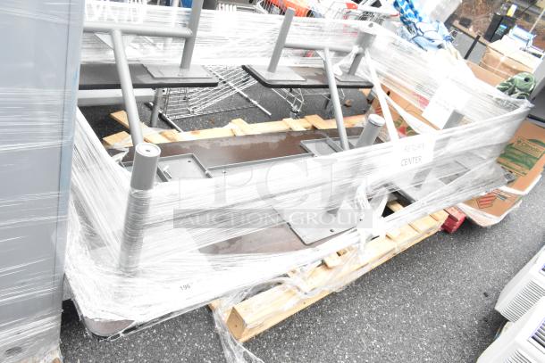 Gray metal table wrapped in plastic on a pallet, labeled "Return Center," showing sturdy legs and rectangular flat surface.
