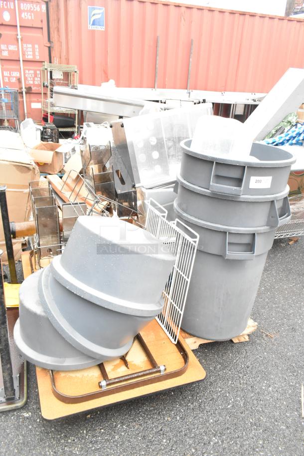 Pallet of various items: gray poly trash cans, lids, folding table. Items appear in used condition.