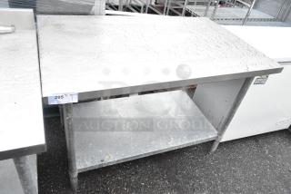 Stainless steel table with under shelf, industrial design, sturdy legs, visible wear, suitable for kitchen or restaurant use.
