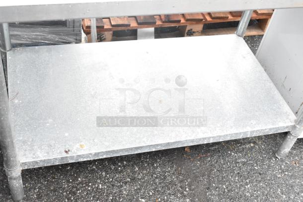 Stainless steel table with an under shelf, sturdy construction, visible wear, ideal for storage or workspace.