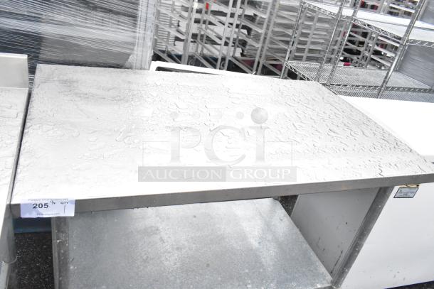 Stainless steel table with under shelf, visible water droplets, lot tag "205", sturdy condition, ideal for kitchen use.