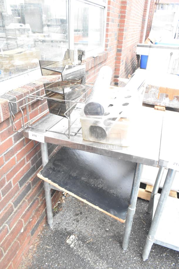 Stainless steel table with metal under shelf, includes assorted contents. Appears in used condition outdoors.