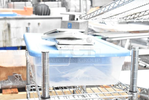 Stainless steel table with metal under shelf, wire shelving, blue-lidded plastic bin, and miscellaneous contents in fair condition.