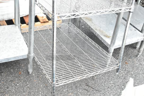 Chrome finish wire shelving unit with four tiers. Visible wear. Buyer must dismantle for shipping. Freight charges apply.