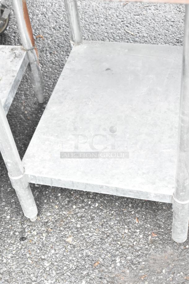 Stainless steel table with metal under shelf, industrial design, sturdy construction, visible wear, suitable for warehouse use.