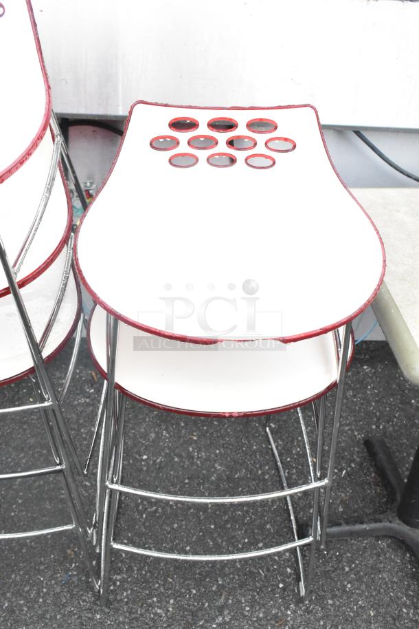 5 white stools with chrome finish legs, red accents, and circular cutouts on seats; slight wear on edges.