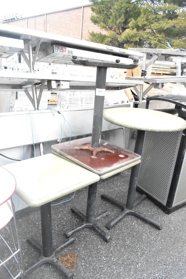 Four various tables, including three dining height and one bar height, with metal bases, showing signs of wear. Label "217" visible.