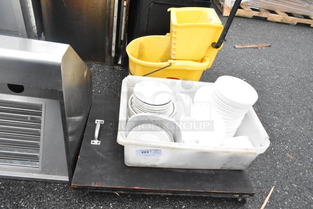Lot of various items including white ceramic plates in a poly white bin, label "223", and a yellow mop bucket.