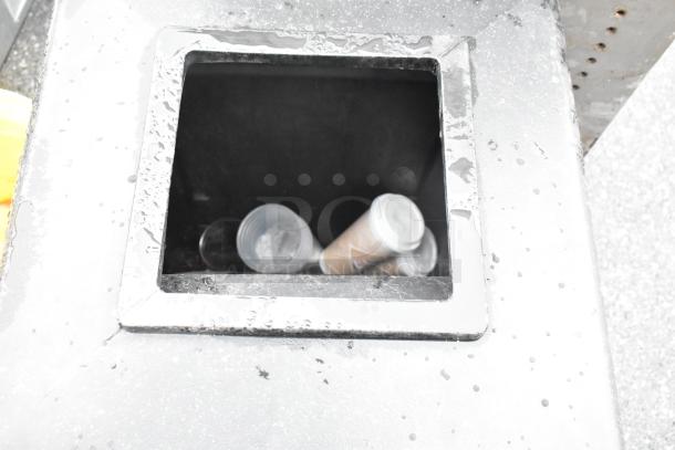 Black poly trash can showing open top with discarded cups inside; exterior shows signs of weathering.