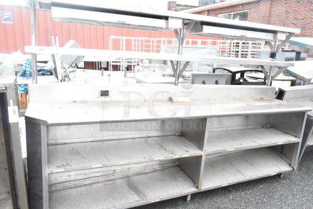 Stainless steel commercial table with 2 food strip warmers, under shelves, over shelves, and visible wear.