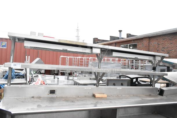 Stainless steel commercial table with two food strip warmers, under shelves, and over shelves in good condition.