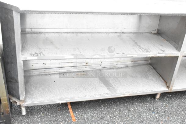 Stainless steel commercial table with under and over shelves. Features two food strip warmers. Visible signs of wear.