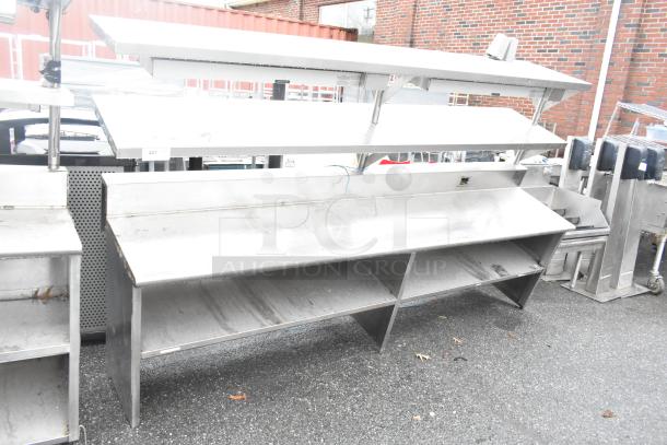 Stainless steel commercial table with two food strip warmers, under shelves, and over shelves, showing visible wear.