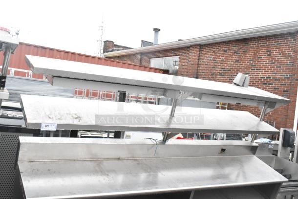 Stainless steel commercial table with two food strip warmers, under shelves, and over shelves, showing visible wear.