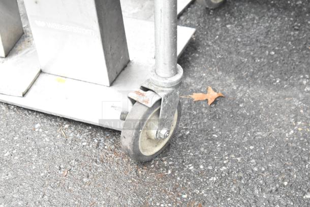 MagiCater charbroiler grill on commercial casters, stainless steel, propane gas powered. Visible: caster and surface wear.