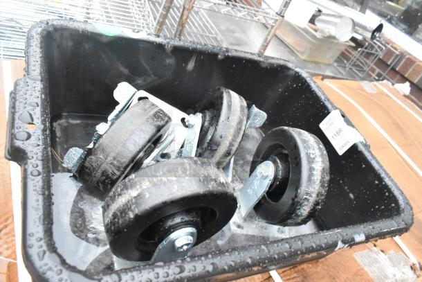 Box containing casters with black wheels and metal attachments, in wet condition. A label reads "JUIC 115R."