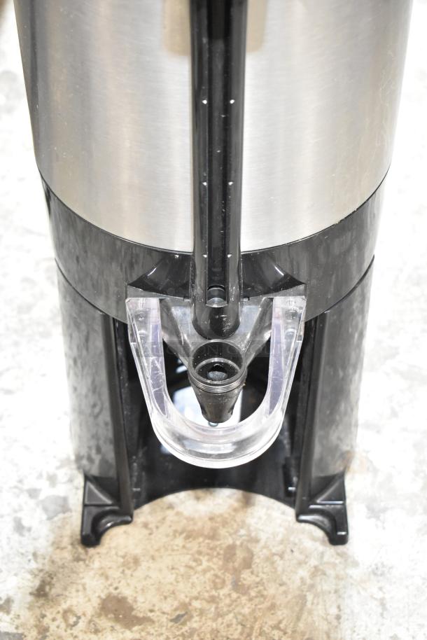 Fetco stainless steel beverage holder dispenser with black plastic base and spout, in good condition, no visible markings.