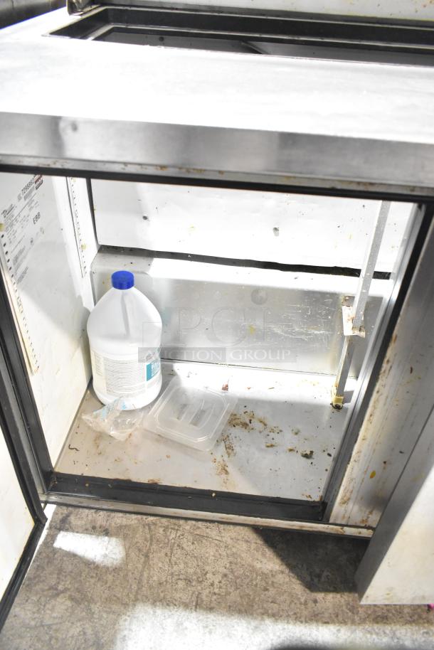 True TSSU-48-12 stainless steel sandwich salad prep table with visible interior shelf, commercial casters, and power label.