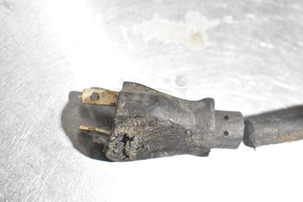 Worn electrical plug with damaged casing, missing prong, and dirty surface on metal background.