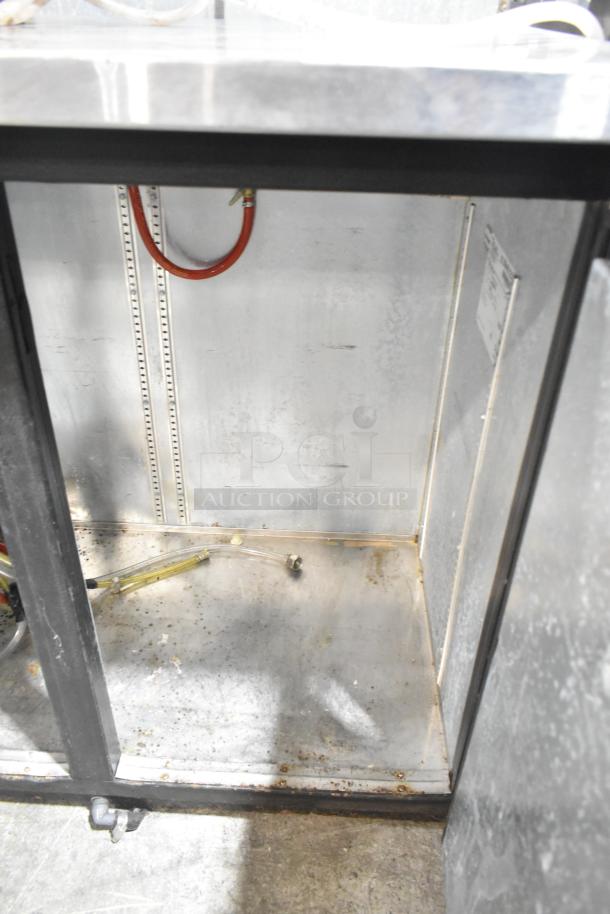 True TDB-24-48 kegerator interior; metal construction, visible piping, moderate wear. Model/voltage label on side.