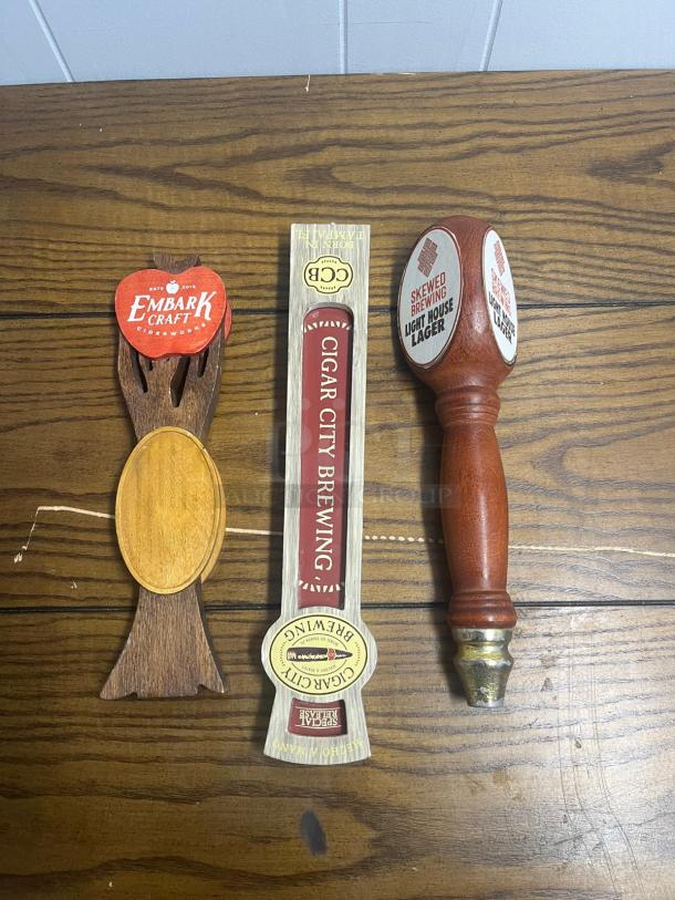Assorted tap handles featuring Embark Craft Ciderworks, Cigar City Brewing, and Skewed Brewing Light House Lager, in used condition.