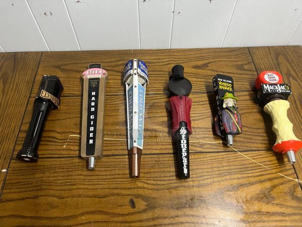 Assorted tap handles on wooden surface; includes Elysian, 1911 Hard Cider, Samuel Adams, Stonepart, New Belgium Voodoo Ranger, and Magic Hat.