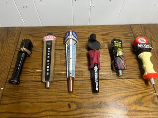 Assorted tap handles on wooden surface; includes Elysian, 1911 Hard Cider, Samuel Adams, Stonepart, New Belgium Voodoo Ranger, and Magic Hat.
