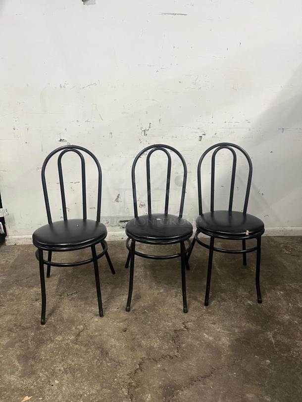 Three cafe dining chairs with black metal frames, padded vinyl seats. Used condition with visible wear on seats.