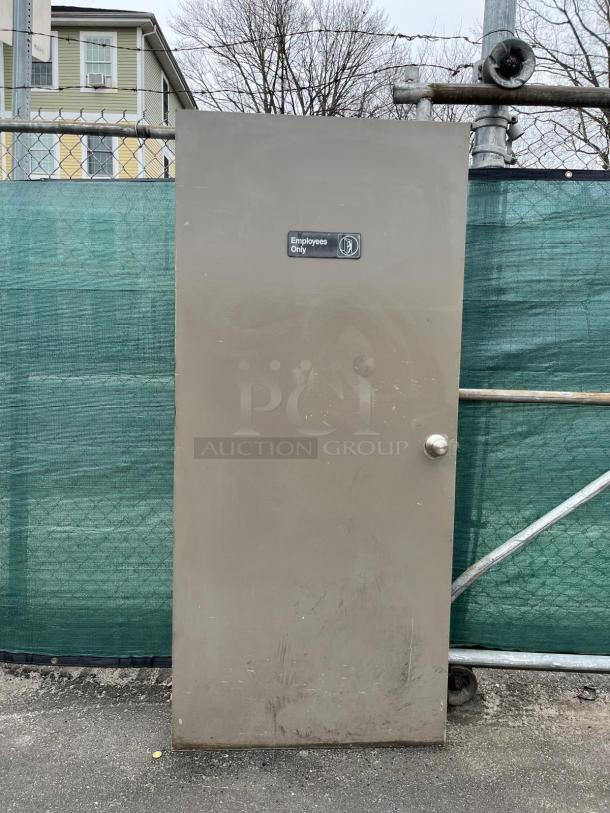 Metal door with "Employees Only" sign, beige color, visible wear and scratches, round handle, sturdy construction.