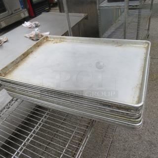 Full-size sheet pans in used condition stacked on metal rack, showing minor wear and discoloration from use.