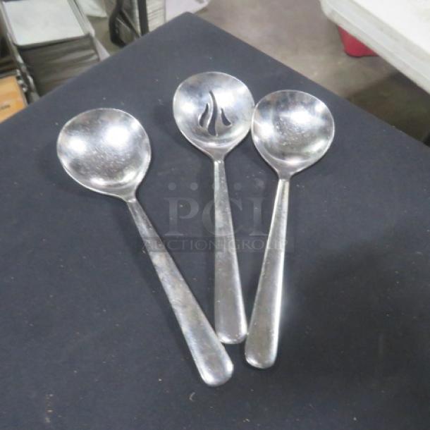 Assorted stainless steel spoons, set of 3. One spoon features slotted design. Minor wear visible, in good condition.