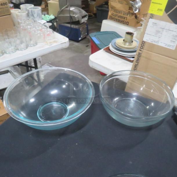 Two clear glass mixing bowls, different sizes, in excellent condition. Displayed on a table amidst various kitchen items.