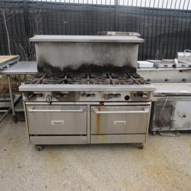 Garland 10-burner natural gas range with stainless steel overshelf on casters. Visible wear, includes oven doors.